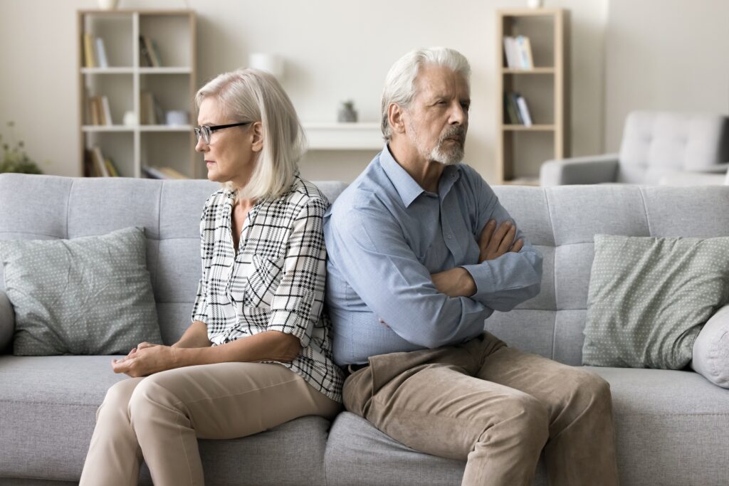 Home interior, couple on couch, back-to-back composition, soft ambient light, editorial travel photo, two upset older adults.