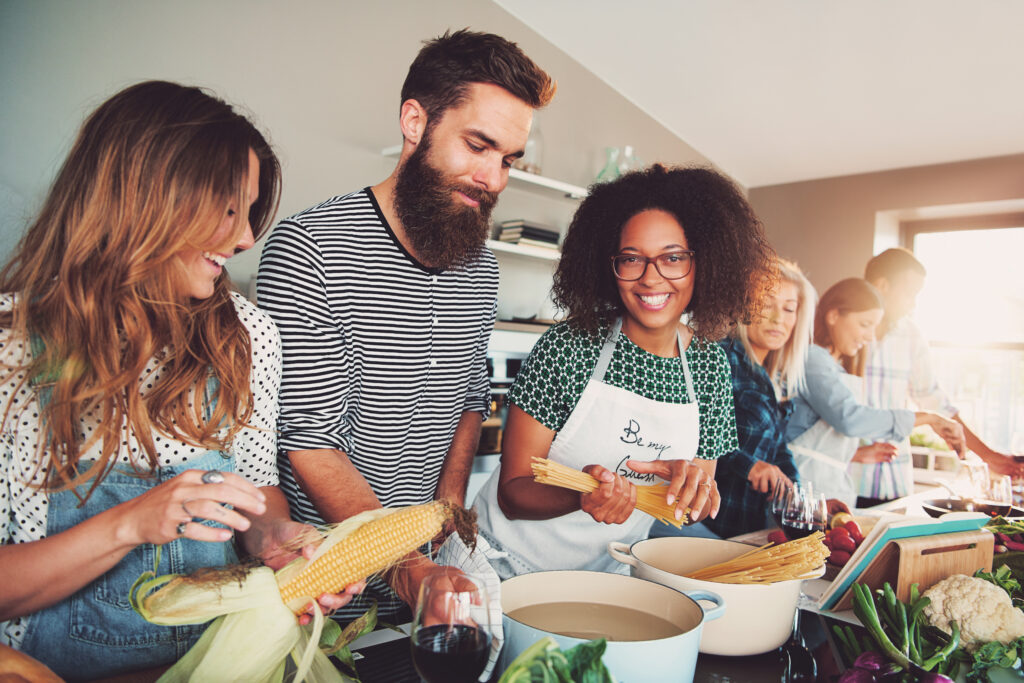 Bright kitchen, friends preparing food, central countertop view, daytime natural light, editorial travel photo, people.
